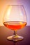 Snifter of brandy in elegant typical cognac glass on colored light disco background