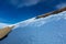 Snow-capped hillside in sunshine under a cloudy, deep-blue sky.