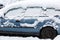 Snow on car wing mirror. Frozen car, blue car covered snow at winter day. Urban scene of city life