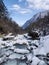 Snow-covered bridge and a tranquil body of water surrounded by mountains and lush trees