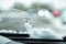 Snow-covered car windshield with melted snow drops and windshield wipers. Blurred lights of passing cars and the city street on