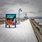 Snow covered dock of the fishing pier on a bright winter day and vivid sea creatures on a billboard