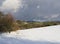 Snow covered meadow with decidouous trees and conifer forest and hills with lookout tower, blue sky. Winter landscape in