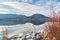 Snow covered mountain and clouds reflected in calm water of lake with rocky shore and wild rosehips in foreground