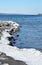 Snow covered rocky shoreline in late winter, blue sky and hills