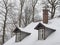 snow covered roof with brick chimney and bay bow window with icicles and bare tree background