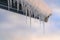 Snow covered roof with row of icicles against sky