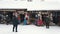 Snow-covered small shops with people wearing winter clothes and busy shopping.