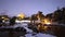 Snow covered stone bridge over pond in illuminated Japanese garden at dawn