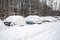 Snow-covered street road and cars under the snow. Heavy snowstorm, blizzard traffic. Climate weather disaster. Winter urban scene