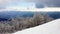 Snow covered trees against distant mountain range & storm clouds