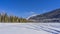 In a snow-covered valley, on the surface of a frozen lake, snowmobile tracks are visible