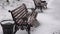 Snow is falling on empty city park. A lonely snow-covered bench stands near sea. Christmas Winter New Year Scenery