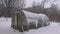 Snow falling on old primitive plastic greenhouse in winter farm