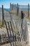 Snow fence lines a path to the beach with a peek of blue ocean and sky in background