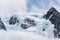 Snow and glacier ice covered rocky mountain peak, with fog below and light white clouds in a blue sky above, Drygalski Fjord, Sout