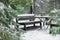 The snow and ice covered benches and a table in the winter park. Coniferous trees grow around. Winter atmosphere concept