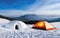 A snow igloo next to a camping tent on a snowy mountain background