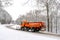 Snow ploughing truck cleans the country road leading through the  forest during a snowfall