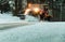 Snow plow at dusk maintains roads in a residential neighborhood during snow storm