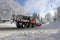 A snow plow with a snow blower drives through the street in winter to clear the high snow away