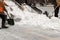 Snow removal on the streets. Close-up of a snowplow and road workers with shovels. People and cars. Abundance of snow. Winter