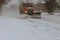 Snow-removing machine cleans the street of the city from the snow in the morning snow-covered trees.