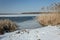 Snow on the shore of a frozen lake and high reeds. Horizon and blue sky