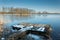 Snow on a wooden fishing pier on the lake. Trees on the shore reflecting in the water