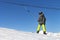 Snowboarder in equipment rises on a lift uphill for skiing against a blue sky