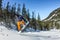 Snowboarder freerider jumping from a snow ramp in the sun on a background of forest and mountains