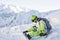 Snowboarder freerider sits on a slope and fastens his snowboard while looking at the mountains. Russia Sochi Rosa Khutor