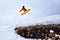 Snowboarder jumping from springboard on a snowy hill with grass.