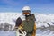 Snowboarder man with orange ski glasses in white helmet posing on top in Alps mountains. On the background of mountains