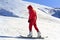 Snowboarder quickly rolls down the mountain in loose snow against a blue sky on a sunny day.