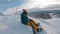 Snowboarder sits high in the mountains on the edge of the slope and looks into the distance.