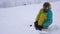 Snowboarder sits on snow, fixing board for snowboard during snowfall