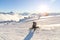 A snowboarder in a ski mask and a backpack is riding on a snow-covered slope leaving behind a snow powder against the