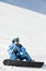 Snowboarder in ski suit sits on snowy hillside