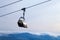 Snowboarder and skier in professional outfit climb up cable car lift up mountains on background of sky, sun and mountain peaks.