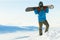 Snowboarder standing at the very top of a mountain and holding snowboard behind his back