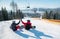 Snowboarders sit on top of ski slope under the lift