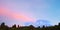 Snowcapped peak of Mount Egmont with red sunset colored clouds start to fill blue sky