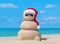 Snowman in Christmas Santa hat and sunglasses at ocean beach