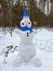 Snowman made of just fallen snow in a blue hat and scarf