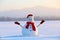 Snowman in red hat and scarf. Christmas scenery. High mountains at the background. Ground covered by snow.