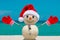 Snowman. Sandy Snowman on the beach. Christmas snowman with red Santa Claus hat and mittens. Smiley Snow man