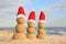 Snowmen made of sand with Santa hats on beach. Christmas vacation