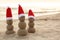 Snowmen made of sand with Santa hats near sea, space for text. Christmas vacation
