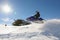 Snowmobile rider jumping machine on sunny hillside